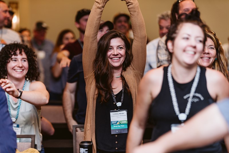woman raises hands in the air and smiles during conference session