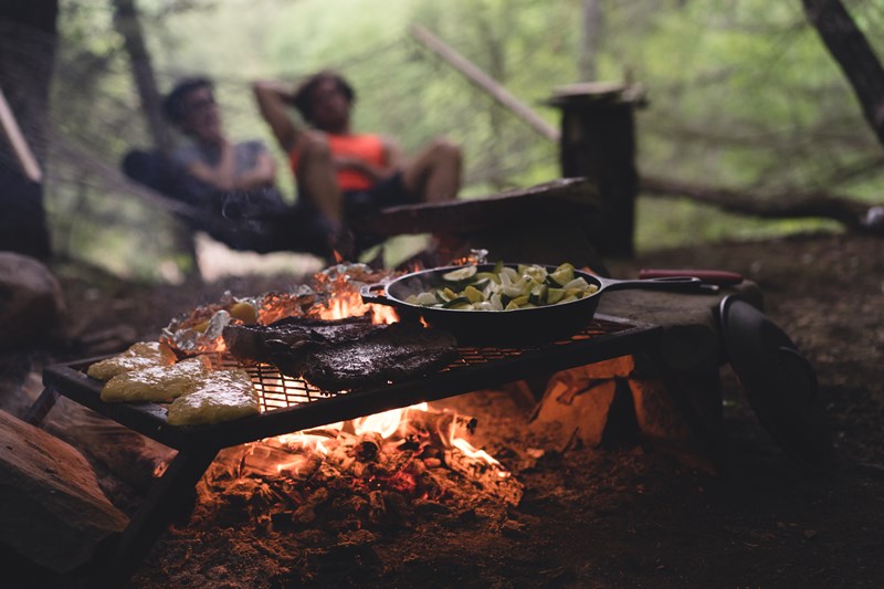 A woman and man sit by a camp fire with delicious food