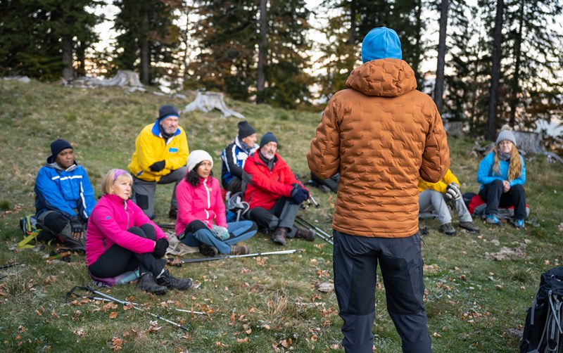 Outdoor recreation guide gives talk to group of participants. Trees and rocks in the background