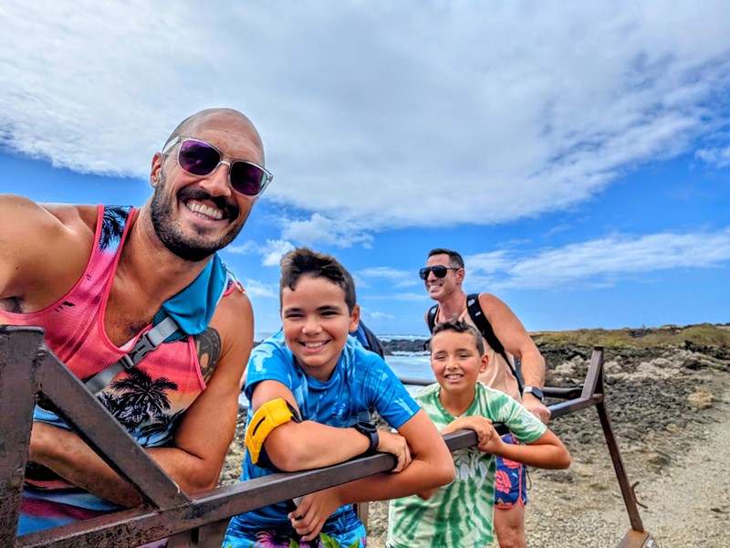 2 dads and their sons smile at the camera on a beach