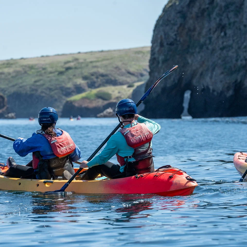 two people kayaking with a small waterfall in the distance